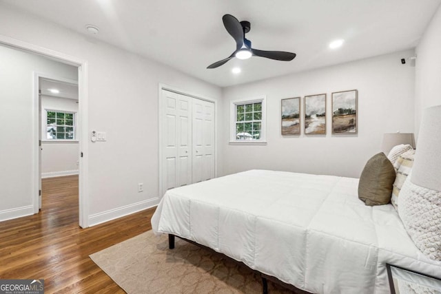 bedroom with multiple windows, dark wood-type flooring, ceiling fan, and a closet