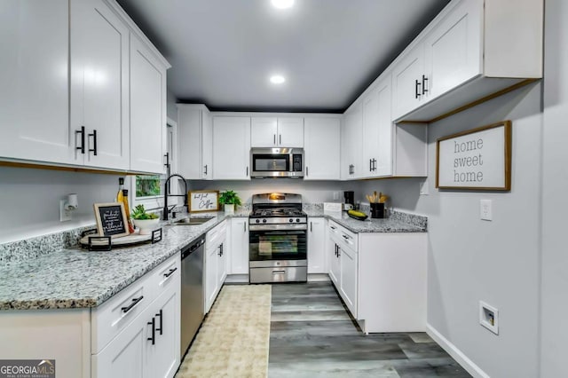 kitchen featuring appliances with stainless steel finishes, white cabinetry, sink, light stone counters, and dark wood-type flooring