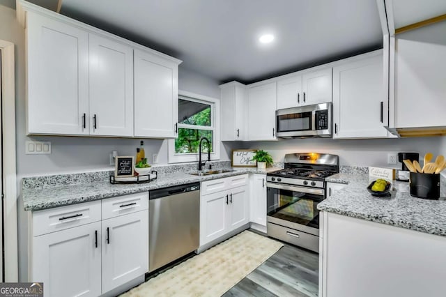 kitchen featuring sink, appliances with stainless steel finishes, light stone counters, white cabinets, and light wood-type flooring