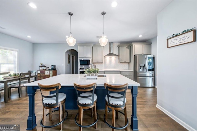 kitchen with stainless steel appliances, hanging light fixtures, gray cabinetry, and wall chimney range hood