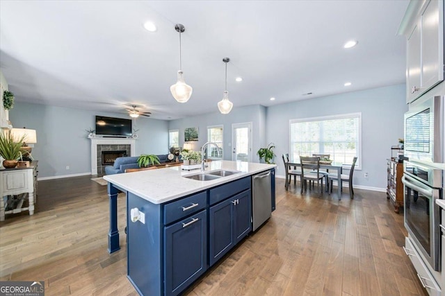 kitchen with blue cabinets, sink, hanging light fixtures, appliances with stainless steel finishes, and an island with sink