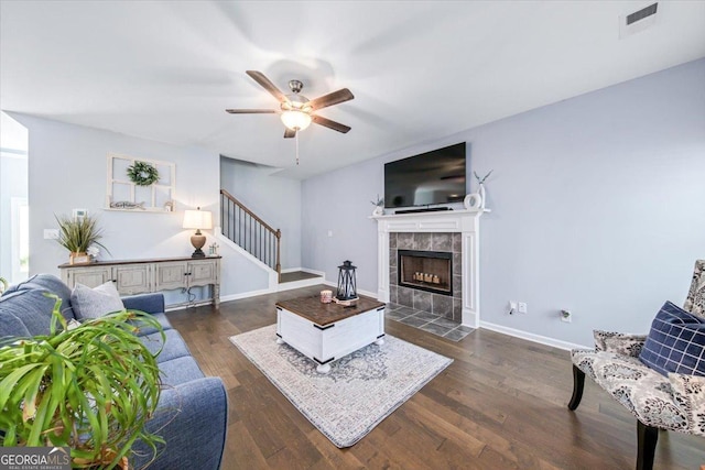 living room featuring a tiled fireplace, ceiling fan, and dark hardwood / wood-style flooring