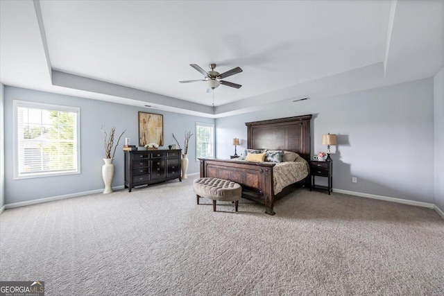 carpeted bedroom with a raised ceiling and ceiling fan