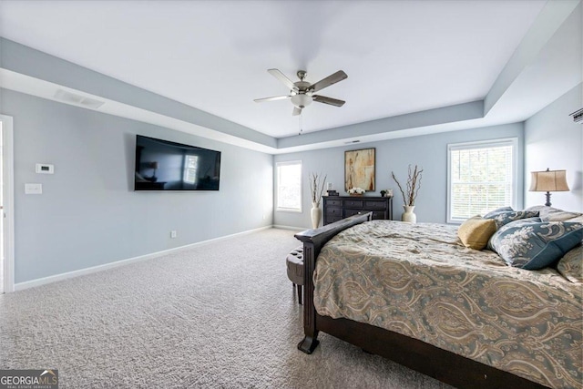 carpeted bedroom with multiple windows, a raised ceiling, and ceiling fan