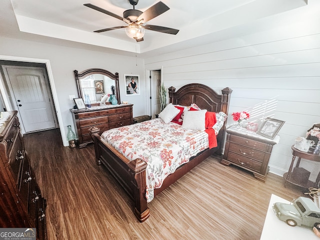 bedroom with hardwood / wood-style flooring, ceiling fan, and a raised ceiling