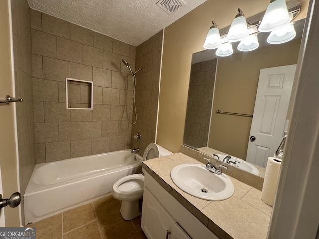 full bathroom featuring tiled shower / bath combo, vanity, a textured ceiling, tile patterned floors, and toilet