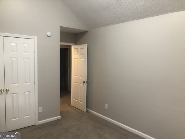 unfurnished bedroom with vaulted ceiling, a closet, a textured ceiling, and dark colored carpet