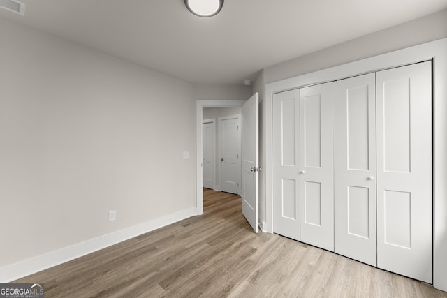 unfurnished bedroom with light wood-type flooring, a closet, visible vents, and baseboards