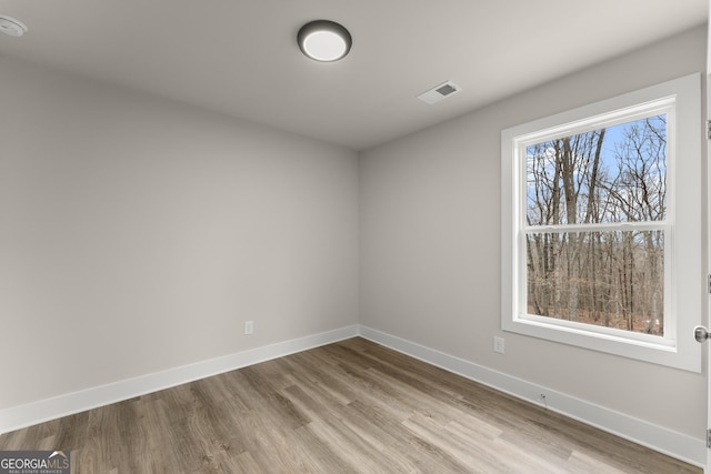 unfurnished room featuring visible vents, baseboards, and wood finished floors