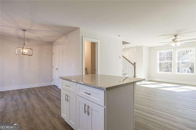 kitchen featuring a center island, hanging light fixtures, dark hardwood / wood-style floors, light stone countertops, and white cabinets