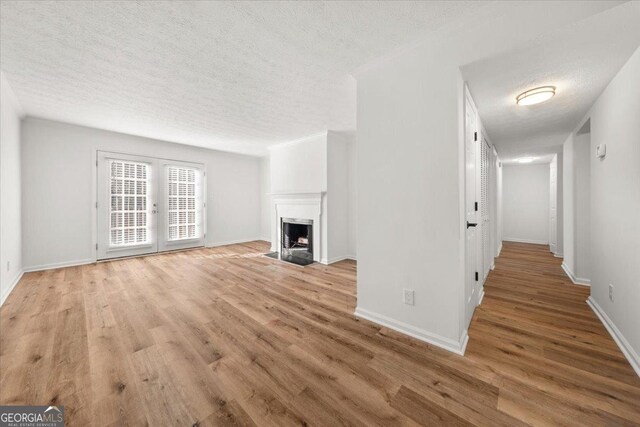 unfurnished living room with a textured ceiling, light hardwood / wood-style floors, and french doors