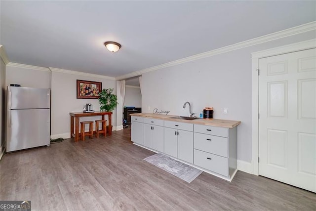 kitchen with sink, crown molding, stainless steel fridge, butcher block countertops, and white cabinetry