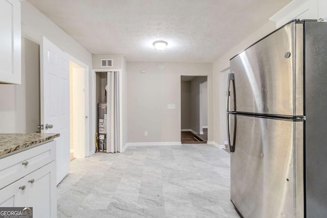 kitchen with stainless steel refrigerator, white cabinetry, light stone counters, and gas water heater