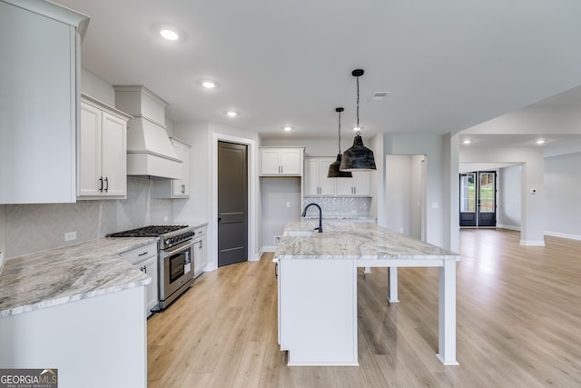 1611 Bethesda Church Rd, Carrollton, GA 30117 - kitchen with stainless steel stove, custom exhaust hood, light wood-type flooring, a center island with sink, and white cabinetry