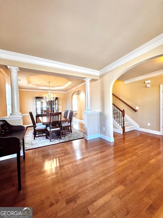 dining space with ornate columns, crown molding, hardwood / wood-style floors, and a tray ceiling