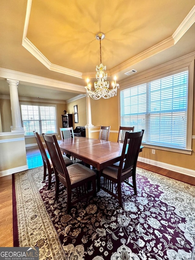 dining room with hardwood / wood-style flooring, a wealth of natural light, decorative columns, and a raised ceiling