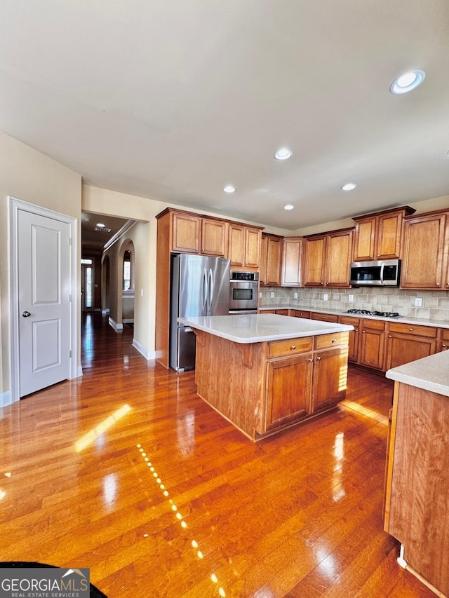 kitchen featuring backsplash, wood-type flooring, stainless steel appliances, and a center island