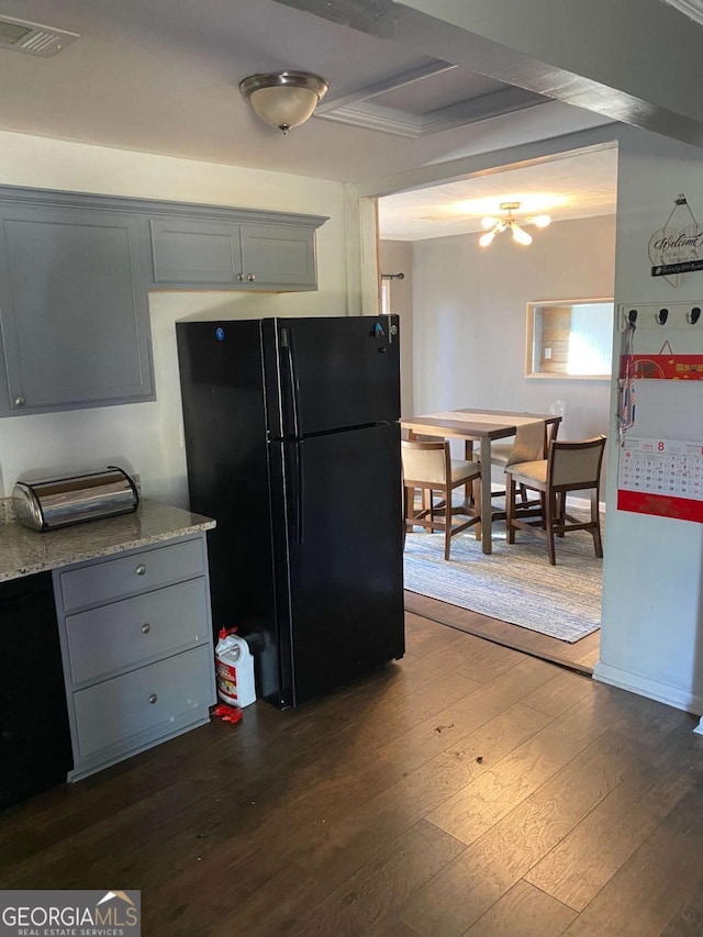 kitchen featuring gray cabinets, black refrigerator, wood-type flooring, ornamental molding, and light stone counters