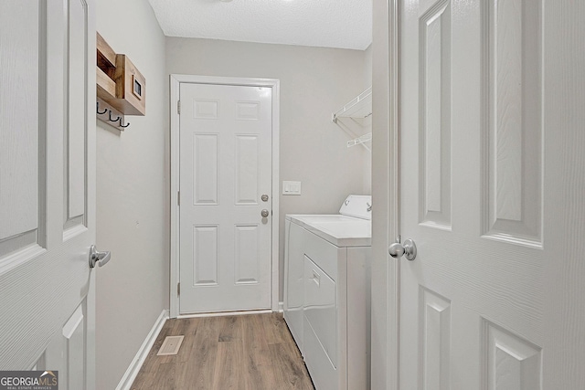 clothes washing area featuring separate washer and dryer, hardwood / wood-style floors, and a textured ceiling