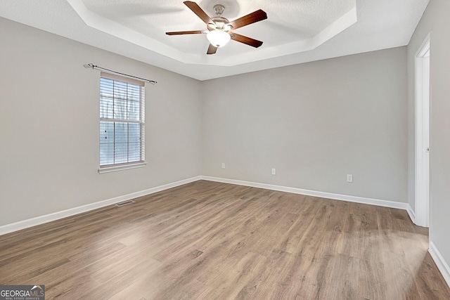 empty room featuring hardwood / wood-style flooring, ceiling fan, a tray ceiling, and a textured ceiling