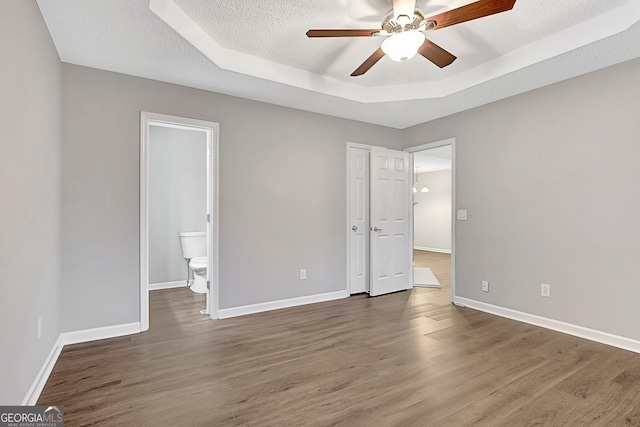 unfurnished bedroom featuring ceiling fan, a tray ceiling, dark wood-type flooring, and a textured ceiling