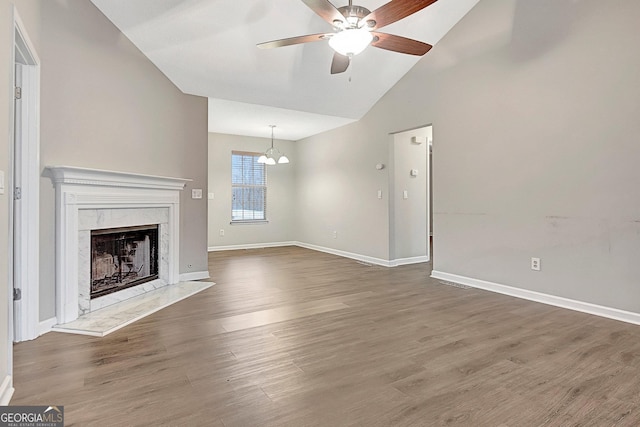 unfurnished living room featuring dark hardwood / wood-style flooring, ceiling fan with notable chandelier, high vaulted ceiling, and a premium fireplace