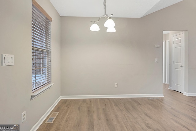 spare room with a chandelier and light wood-type flooring