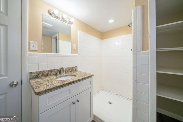 bathroom featuring vanity, a tile shower, tile walls, and backsplash