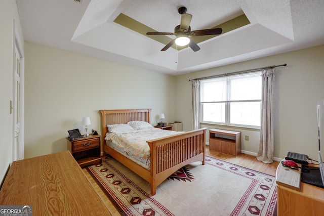 bedroom featuring ceiling fan, a raised ceiling, a textured ceiling, and light wood-type flooring