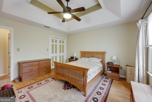 bedroom featuring a tray ceiling, a closet, ceiling fan, and light wood-type flooring