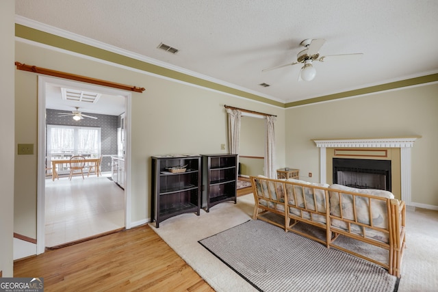 living room featuring hardwood / wood-style flooring, ornamental molding, ceiling fan, and a textured ceiling