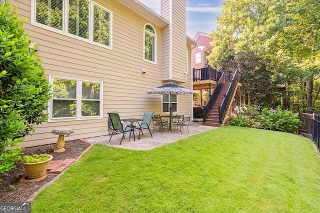 rear view of house featuring a wooden deck, a patio area, and a lawn