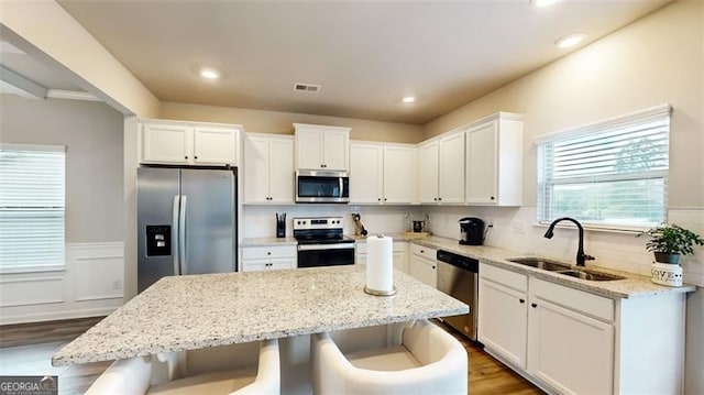 kitchen with appliances with stainless steel finishes, white cabinetry, sink, a center island, and light stone countertops