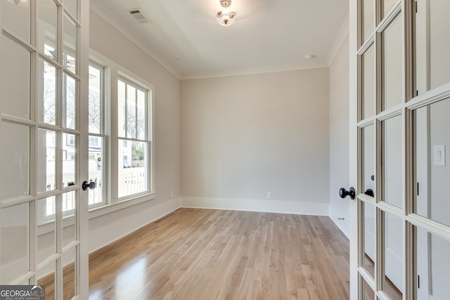 empty room with ornamental molding, light wood-type flooring, and french doors