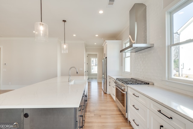 kitchen with pendant lighting, wall chimney range hood, a large island with sink, and appliances with stainless steel finishes