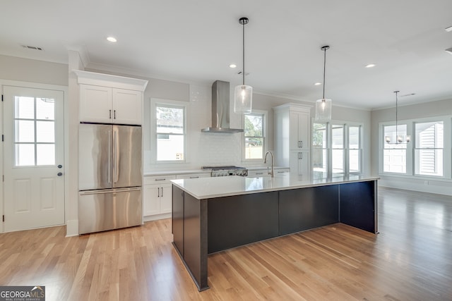 kitchen featuring wall chimney exhaust hood, stainless steel fridge, hanging light fixtures, and white cabinets