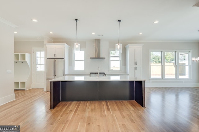 kitchen featuring high end fridge, white cabinets, a large island with sink, and wall chimney exhaust hood