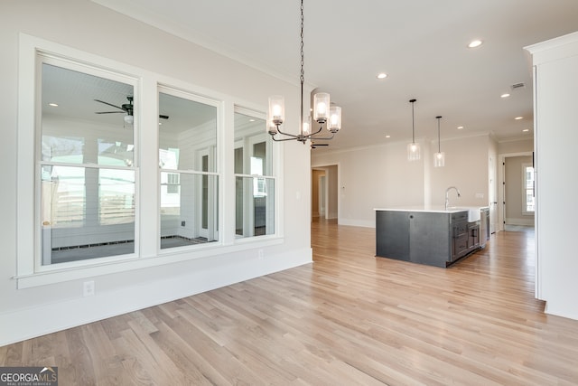 unfurnished dining area with sink, ceiling fan with notable chandelier, light hardwood / wood-style flooring, and ornamental molding