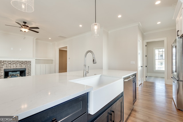 kitchen featuring sink, appliances with stainless steel finishes, hanging light fixtures, ornamental molding, and light stone countertops