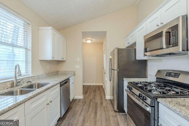 kitchen featuring sink, white cabinets, light stone counters, light hardwood / wood-style floors, and stainless steel appliances