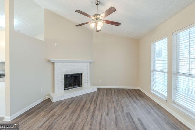 unfurnished living room with vaulted ceiling, a brick fireplace, a textured ceiling, ceiling fan, and hardwood / wood-style floors