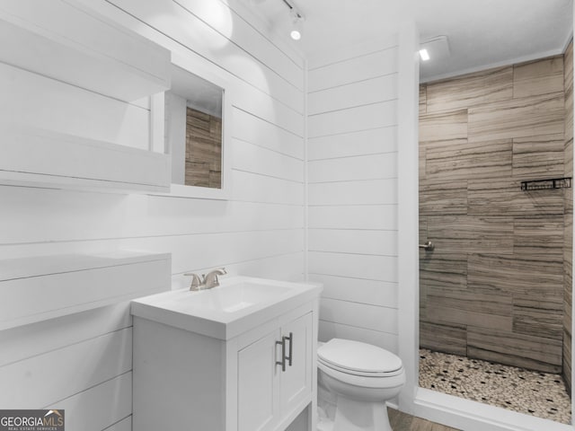 bathroom featuring toilet, vanity, wooden walls, and a tile shower