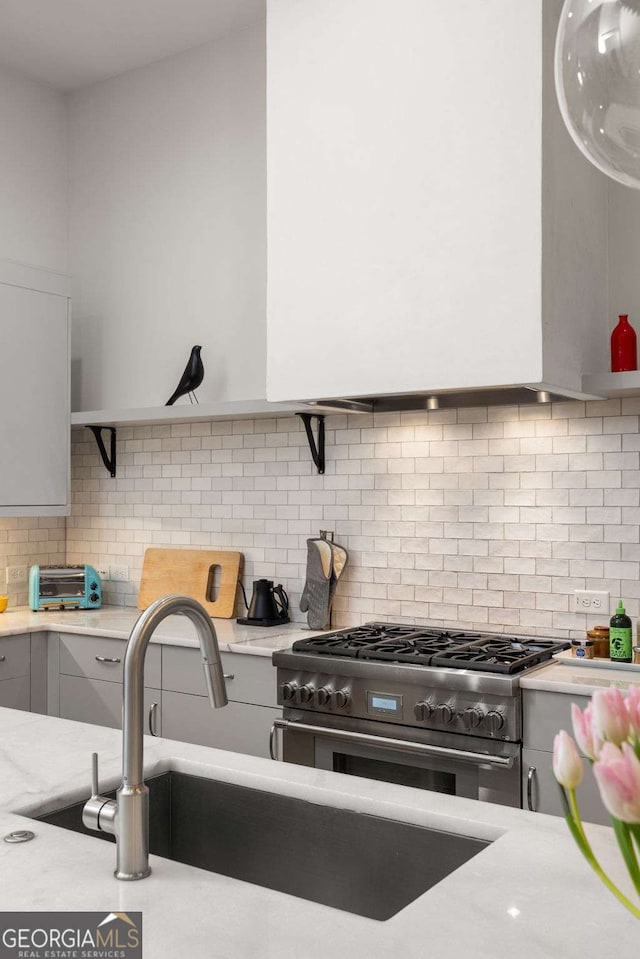 kitchen featuring stainless steel range, light stone countertops, sink, and decorative backsplash