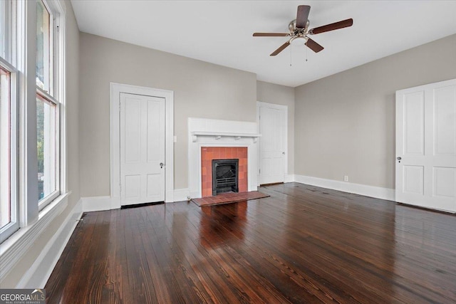 unfurnished living room with a tiled fireplace, dark wood-type flooring, and ceiling fan