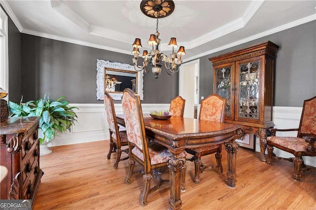 dining space featuring an inviting chandelier, a tray ceiling, crown molding, and light wood-type flooring