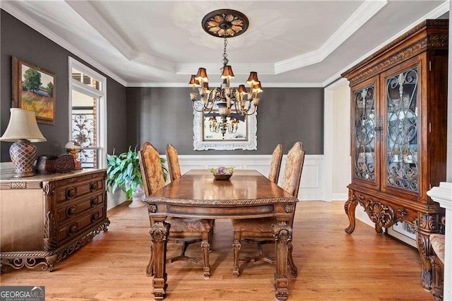 dining area featuring a raised ceiling, crown molding, a chandelier, and light hardwood / wood-style floors