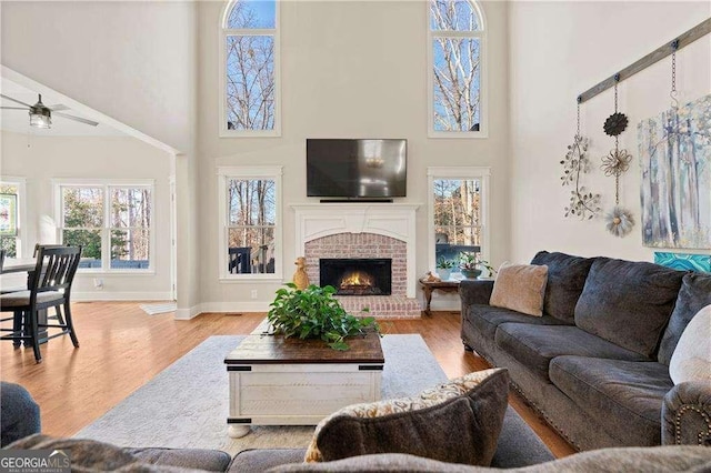 living room featuring a high ceiling, a brick fireplace, and light wood-type flooring