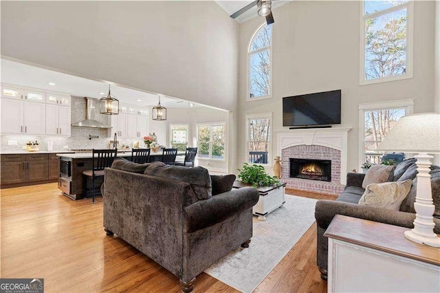 living room with a towering ceiling, light hardwood / wood-style floors, and a brick fireplace