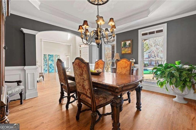 dining space with ornamental molding, a notable chandelier, light hardwood / wood-style floors, and a tray ceiling