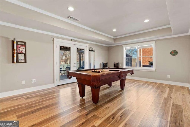 recreation room featuring a raised ceiling, crown molding, light wood-type flooring, and french doors